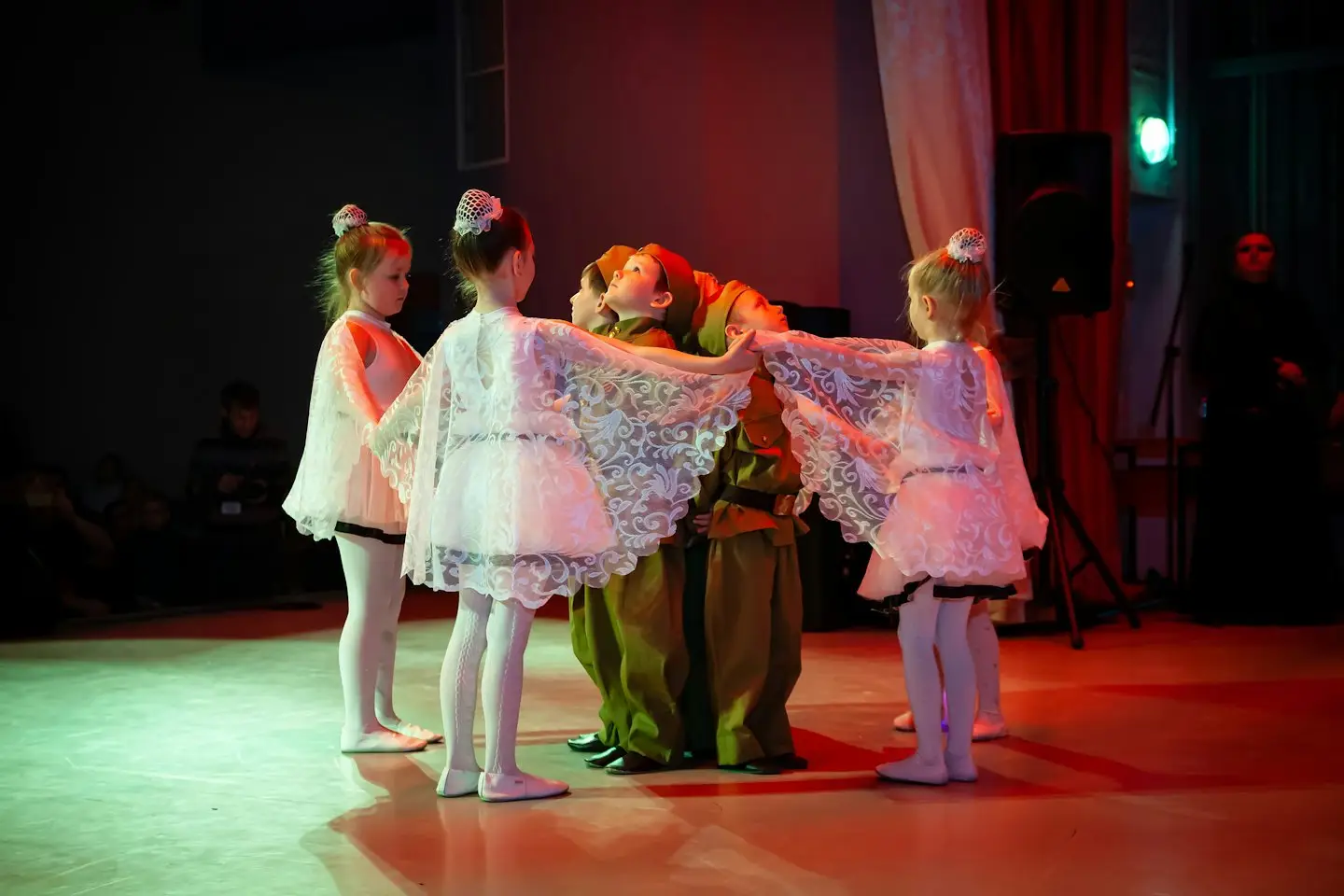 Kinderen in nette kostuums dansen in een cirkel op een podium.